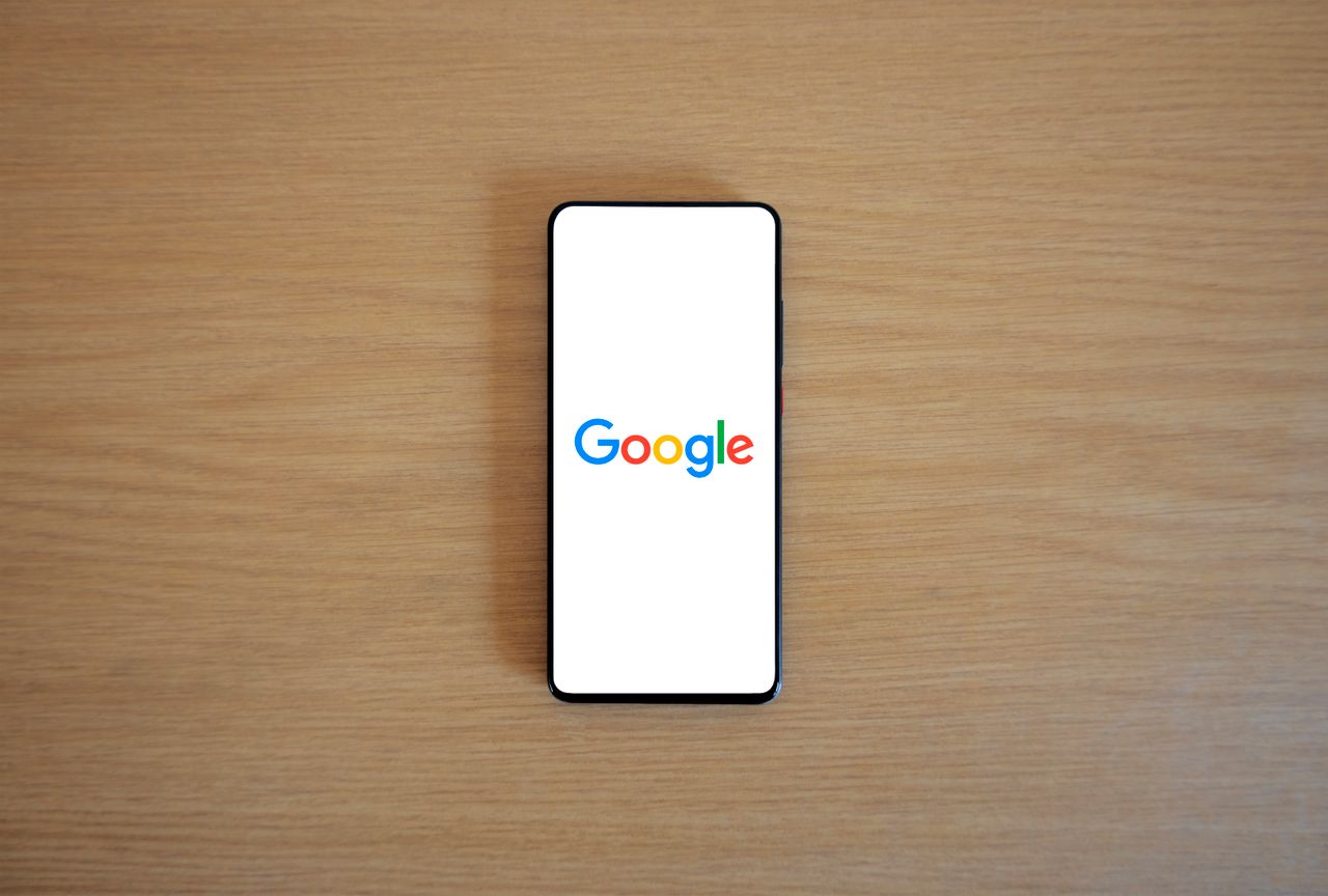 A smartphone showing the Google homepage lying on a wooden surface, seen from above.
